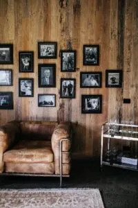 Various old framed photos hanging on wooden wall near comfortable armchair in vintage styled room with carpet an decorations